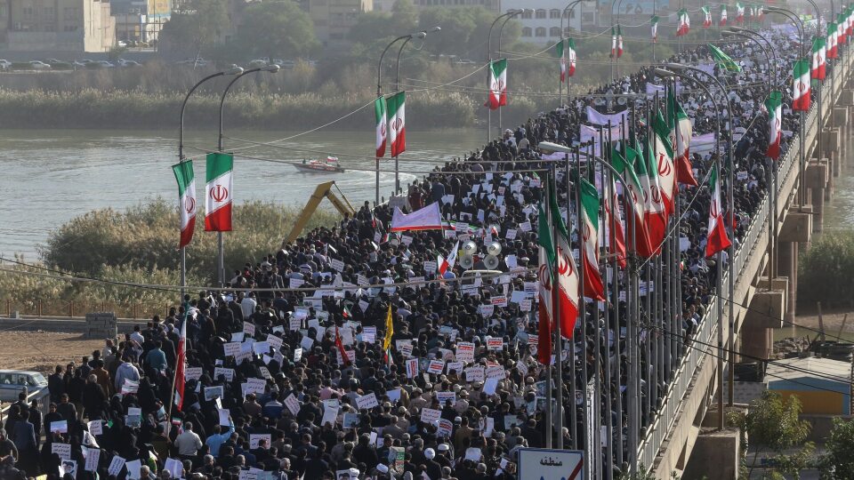 A large crowd marches across a bridge in Iran carrying national flags